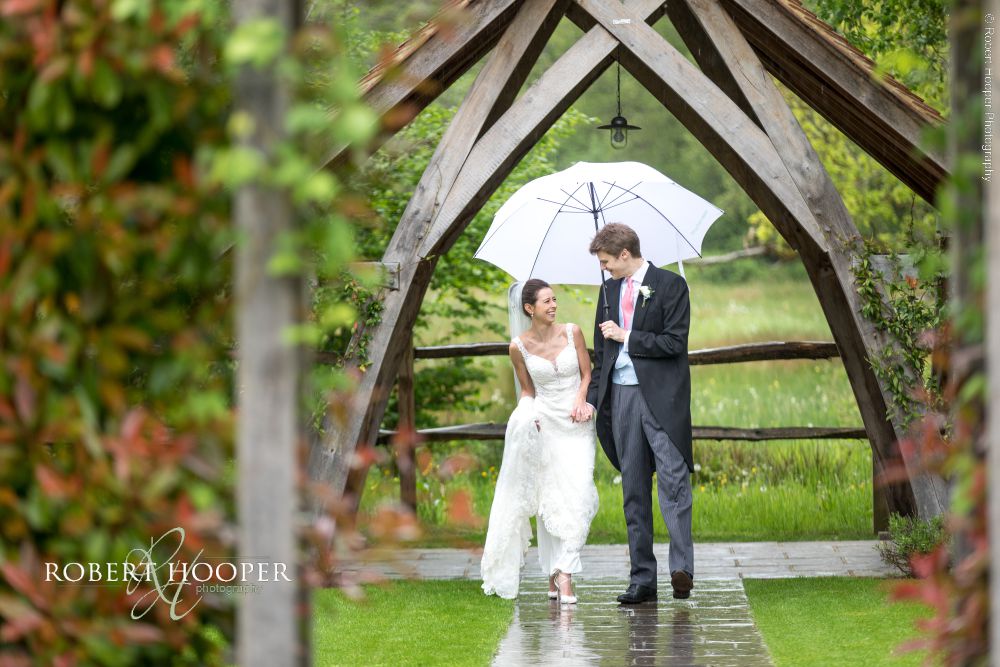 Millbridge Court wedding photography Surrey bride and groom holding hands under umbrella on rainy wedding day at Millbridge Court